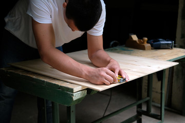 Carpenter marking straight line on plywood sheet using spirit level in carpentry workshop. Measuring, drawing line, DIY concept.