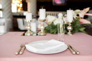 The wedding table setting for the newlyweds is decorated with fresh flowers of carnation, rose, anthurium and eucalyptus leaves. Silver candlesticks, white candles. Wedding floristry. Close-up details