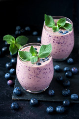 Blueberry smoothie in  glass with mint leaves on dark background