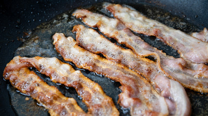 Slices of bacon baking on the pan, salt-cured pork
