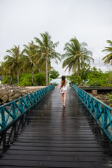 Fototapeta na wymiar A young girl in a dress walking on a wooden bridge. The island is cloudy