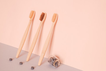 Bamboo toothbrush and dry tooth paste or toothpaste tablets on pink blue background. Zero waste, ecological concept.