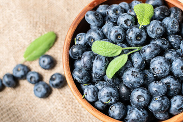 Fresh organic ripe blueberries in clay bowl isolated on rustic sackcloth background.