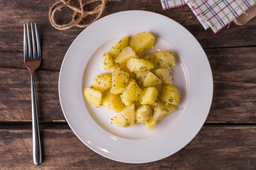 Boiled potatoes with dill on white plate on rustic wood table
