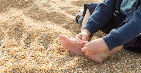 Child playing with the toes and feeling the texture of the beach sand, sensory experience
