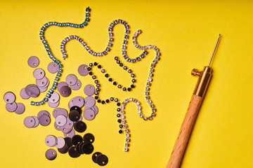 Embroidery products and tools. Black sequins, rhinestones and Luneville hook on a yellow background