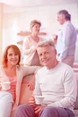 Portrait of smiling mature couple holding coffee while sitting against friends at home