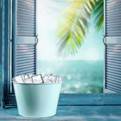 Cold ice in metal container with free space for your product or bottle. Blue retro window sill. Summer landscape of sea with green coconut palm leaf. 