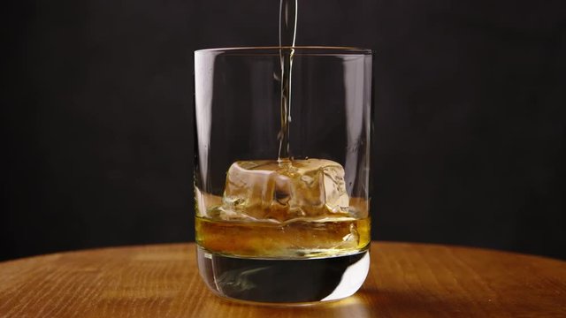 Delicious golden scotch whiskey being poured into glass by barman with perfect ice cube for a celebration drink