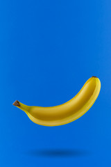 A single fresh, yellow, ripe, flying banana casts a shadow isolated on a blue background. Min mod, flatlay. The concept of ideas of creative thinking of various creative abilities of albinos.