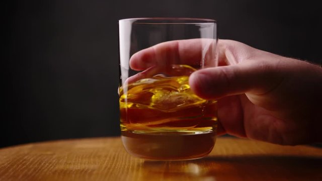 Delicious golden scotch whiskey being swirled in glass by barman with perfect ice cube for a celebration drink