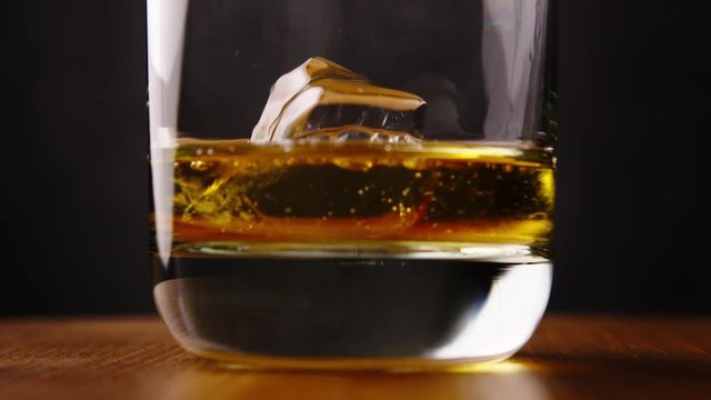 Delicious golden scotch whiskey being poured into glass by barman with perfect ice cube for a celebration drink
