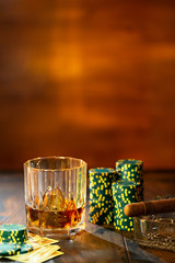 Whisky with ice, cigar and cards with game chips on wooden background