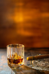 Whisky with ice and cigar on wooden background