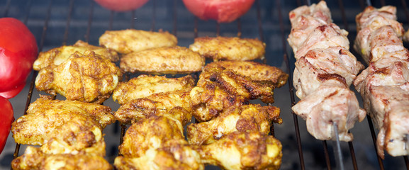 Barbecue shashlik kebab with winglets and tomatoes with roasted pepper in chargrill semifinished on skewer side view closeup