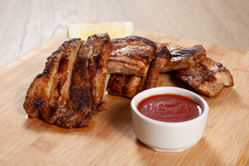 Delicious grilled ribs with red sauce on wooden board