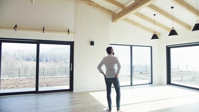 Rear view of mature man standing in unfurnished house, moving in new home concept.