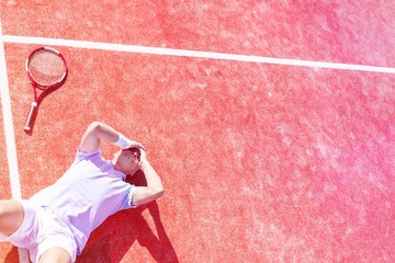 High angle view of disappointed mature man with head in hands while lying by tennis racket on court...