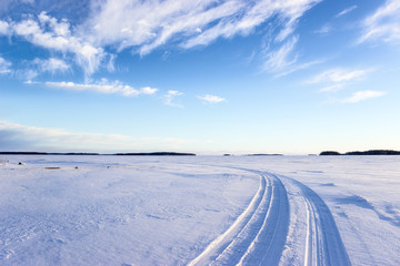 Fototapeta na wymiar Road on snow and ice of frozen lake, tracks going to distance, sunny cold weather