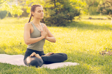 Young Caucasian woman doing yoga in the Park. Sitting in Lotus position