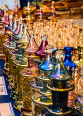 Close together standing richly decorated and colored perfume flacons made of glass in the light of the setting sun.