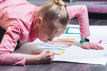 Young girl draws on the floor with paints on paper