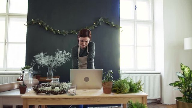 Young creative woman in a flower shop, using laptop. A startup of florist business.