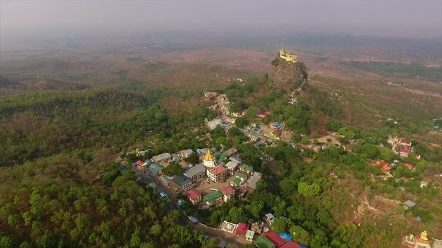 Wide high- angle panning shot of Mount Popa monastery, buildings, villages, infrastructure, and natural landscape, Bagan, Myanmar