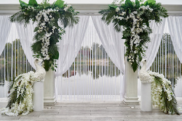 Luxury wedding arch decorated with palm leaves, orchid flowers and floral peacocks outdoors, copy...