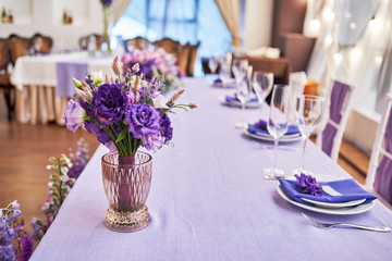 Bridal bouquet of purple flowers in glass vase on wedding banquet table in restaurant, copy space