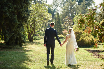 Happy bride and groom holding hands and walking in garden on wedding day. Wedding couple in love, newlyweds, copy space