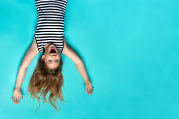 Laughing girl laying on blue backdrop up side down. Smiling, happy child. Childhood memories....