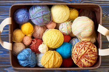 Knitting pattern of colorful yarn wool in box on blue wooden background. Top view. Knitting...