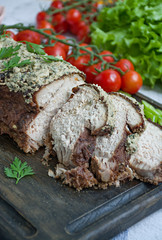 Baked pork chopped in a walnut and mint sauce on a cutting board with fresh herbs and vegetables. Light background.