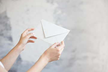 Close-up girl holds with two hands a white envelope wedding invitation notice on a gray background.
