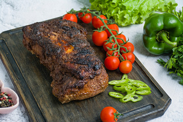 Baked pork chopped in a walnut and mint sauce on a cutting board with fresh herbs and vegetables. Light background.