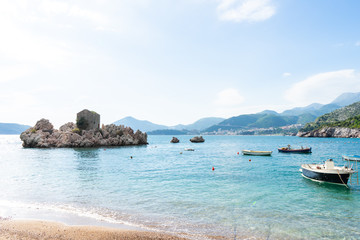 Obraz premium Special different rock in the adriatic sea in a small coast village in Budva. Small boats in the beach in turquoise blue water and amazing landscape. Summer concept