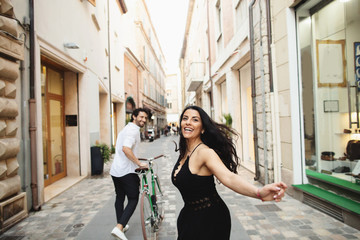 Beautifully dressed man and woman are walking in the old city with a bicycle. Love story in Rimini,...