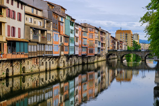 View of the Castres architecture on houses along the Agout river.  Angled view from side of river with house reflection  leading to old bridge.  Castres, France May 2019