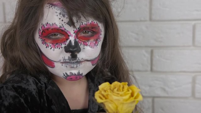 Scary party. Child for halloween with a rose. Little girl with scary halloween make-up with dry rose. Halloween child.