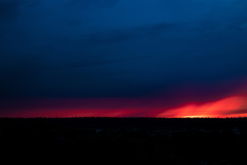 Obraz premium Evening sky at sunset background. Dark clouds hanging above horizon. Majestic cloudscape in blue, orange, violet shades. Grey cloudlets bringing rain. Countryside skyline in twilight time