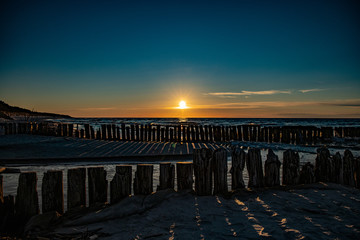 colorful sunset over the Polish Baltic sea with dark sky clouds and breakwater