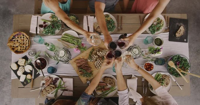 Friends Having A Dinner Party Together, Top Down View Of Dinner Table With Six Friends Cheersing With Wine Glasses, Raising A Toast