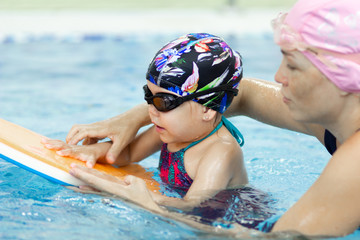 Little girl and her mother making excercises with float board in the swimming pool