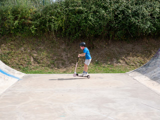 Fototapeta premium Young boy riding a scooter on a skate park