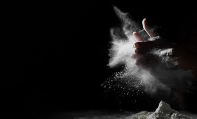woman chef hand clap with splash of white flour and black background with copy space.