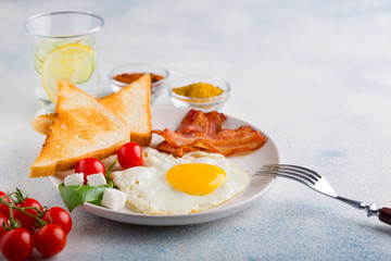 Fried egg with bacon, toast, tomatoes and a glass of mineral water with lemon and cucumber on a white background. English breakfast. with copy space for your text