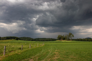 Fototapeta na wymiar Field, fence, hill and stormy clouds landscape