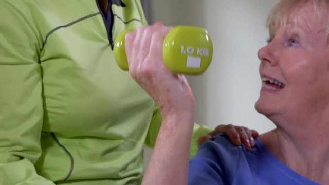 Female Physiotherapist Helping Senior Woman To Lift Hand Weights