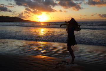 Mujer caucásica en contra luz en la playa con atardecer de naranja intenso. Las palmas de gran...
